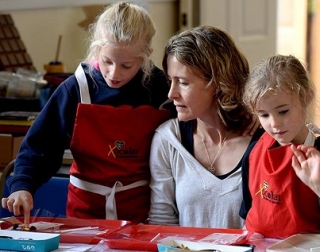 A woman and two girls wearing aprons sit and stand behing a table and make chocolate A woman and two girls wearing aprons sit and stand behing a table and make chocolate