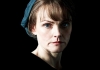 A woman in a blue cap looks intensely at the camera, on a black background. A woman in a blue cap looks intensely at the camera, on a black background.