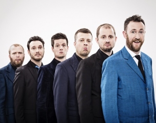 Six men wearing suits stand in a row, pulling faces at the camera. Six men wearing suits stand in a row, pulling faces at the camera.