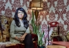 A woman sits on a sofa in a room with patterned wallpaper behind her A woman sits on a sofa in a room with patterned wallpaper behind her