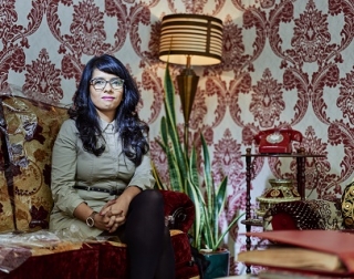 A woman sits on a sofa in a room with patterned wallpaper behind her A woman sits on a sofa in a room with patterned wallpaper behind her