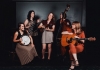 A group of women hold their instruments and laugh and talk together, in a dark room with a patterned carpet. A group of women hold their instruments and laugh and talk together, in a dark room with a patterned carpet.