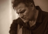 A close-up, sepia toned image of a man looking down and playing the guitar A close-up, sepia toned image of a man looking down and playing the guitar