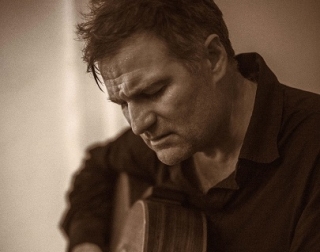A close-up, sepia toned image of a man looking down and playing the guitar A close-up, sepia toned image of a man looking down and playing the guitar