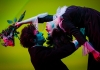 Women leans backwards, holding flowers, whilst a man supports her back and looks into her closed eyes. Set against a green background. Women leans backwards, holding flowers, whilst a man supports her back and looks into her closed eyes. Set against a green background.