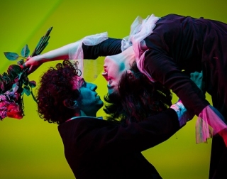Women leans backwards, holding flowers, whilst a man supports her back and looks into her closed eyes. Set against a green background. Women leans backwards, holding flowers, whilst a man supports her back and looks into her closed eyes. Set against a green background.
