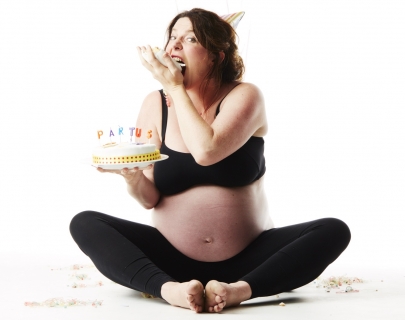 A pregant lady wearing black leggings and a black bra sits cross legged on the floor eating cake A pregant lady wearing black leggings and a black bra sits cross legged on the floor eating cake