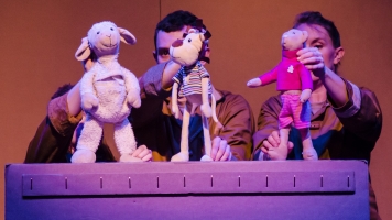 toys on top of a cardboard box being controlled like puppets by actors on stage toys on top of a cardboard box being controlled like puppets by actors on stage