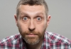 Comedian Dave Gorman staring at the camera wearing a red checked shirt Comedian Dave Gorman staring at the camera wearing a red checked shirt