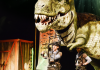 Two actors dressed as explorer with a T-Rex behind them Two actors dressed as explorer with a T-Rex behind them