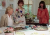 Three smiley middle aged women holding wine glasses and standing around a kitchen table in a room full of light Three smiley middle aged women holding wine glasses and standing around a kitchen table in a room full of light