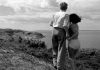 Black and white. A man and a woman look out over the ocean from a cliff. Black and white. A man and a woman look out over the ocean from a cliff.