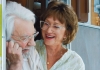 A retired couple wearing glasses sit in the doorway of their Winnebago, laughing. A retired couple wearing glasses sit in the doorway of their Winnebago, laughing.