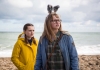 Two young girls standing on a pebbled beach looking inland, one wears rabbit ears, the other a yellow coat Two young girls standing on a pebbled beach looking inland, one wears rabbit ears, the other a yellow coat