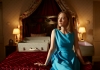 A young woman in a blue dress sits on a bed looking out a window A young woman in a blue dress sits on a bed looking out a window