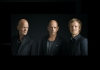 Three men wearing dark suits standing against a black background Three men wearing dark suits standing against a black background
