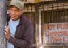 Musician Robert Cray leans against a post, wearing a green cap and a blue t shirt, outside a closed diner. Musician Robert Cray leans against a post, wearing a green cap and a blue t shirt, outside a closed diner.