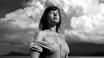 Black and white. A woman stands against a sunny sky with her eyes closed. Black and white. A woman stands against a sunny sky with her eyes closed.