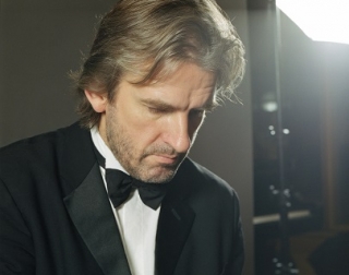 Pianist Barry Douglas sits at a piano, wearing a black suit and a black bow tie. Pianist Barry Douglas sits at a piano, wearing a black suit and a black bow tie.
