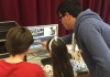 Two children work on editing a video, directed by a workshop leader. Two children work on editing a video, directed by a workshop leader.