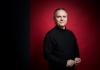 Conductor Sir Mark Elder in a black outfit against a red background Conductor Sir Mark Elder in a black outfit against a red background