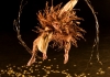 A dancer dressed in brown and gold jumping in the air against a black background A dancer dressed in brown and gold jumping in the air against a black background