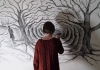 A girl in a red jumper drawing a dark forest on a white wall A girl in a red jumper drawing a dark forest on a white wall