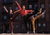 Three men doing high kicks with their arms in the air with a building behind them. The man in the middle wears a bright red shirt. Three men doing high kicks with their arms in the air with a building behind them. The man in the middle wears a bright red shirt.