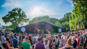 A fish-eye view of a festival stage, with a audience in front of it, on a summer's day. A sign on the right says, 'Lunar'. A fish-eye view of a festival stage, with a audience in front of it, on a summer's day. A sign on the right says, 'Lunar'.