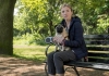 A blonde woman sits on a bench holding a pug. A blonde woman sits on a bench holding a pug.