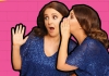 Two images of Lucy Porter wearing a blue sparkly top. Lucy Porter whispers into Lucy Porter's ear against a bright pink and yellow background. Two images of Lucy Porter wearing a blue sparkly top. Lucy Porter whispers into Lucy Porter's ear against a bright pink and yellow background.