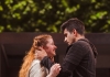 a girl with ginger hair and a white jacket and boy with black hair and a black jacket embrace in front of a green background a girl with ginger hair and a white jacket and boy with black hair and a black jacket embrace in front of a green background