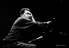 Black and white image of Abdullah Ibrahim sitting at a piano. Black and white image of Abdullah Ibrahim sitting at a piano.
