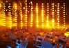 A large room filled with rocking chairs are lit by many hanging orange bulbs A large room filled with rocking chairs are lit by many hanging orange bulbs