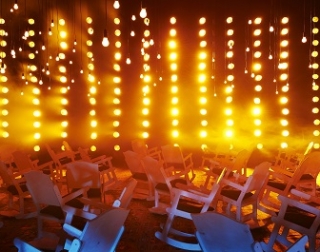 A large room filled with rocking chairs are lit by many hanging orange bulbs A large room filled with rocking chairs are lit by many hanging orange bulbs
