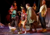 Four performers, two female and two male, in colourful clothes, stand in a line behind a puppet of a white duck Four performers, two female and two male, in colourful clothes, stand in a line behind a puppet of a white duck