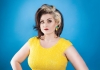 Kiri stands in front of a bright blue background wearing a bright yellow dress Kiri stands in front of a bright blue background wearing a bright yellow dress