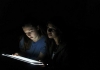 Two faces are lit by an electronic screen against total blackness Two faces are lit by an electronic screen against total blackness