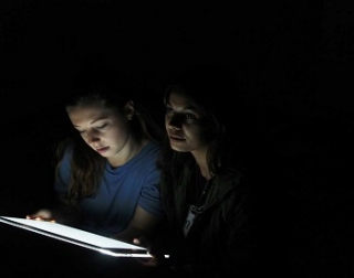 Two faces are lit by an electronic screen against total blackness Two faces are lit by an electronic screen against total blackness
