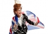 An elderly woman with stained teeth, bird's nest red hair and glasses smiles, whilst wearing a black embroidered jacket and a Union Jack flag. An elderly woman with stained teeth, bird's nest red hair and glasses smiles, whilst wearing a black embroidered jacket and a Union Jack flag.